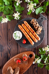 Grilled sausages with mushrooms on a round dark board with sandwiches with baked cherry and sauce