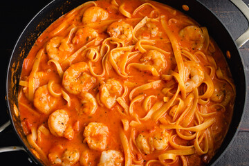 Shrimp and Pasta in Tomato Cream Sauce in a Saute Pan: A skillet full of shrimp and fettuccine pasta noodles in a creamy tomato sauce