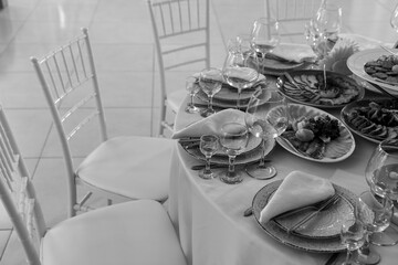 Table and chairs with wine glass, plates full serving. Napkins and cutlery. Low light. Selective focus. Ready to party, celebrate. Restaurant services, public catering enterprises. Black and white.