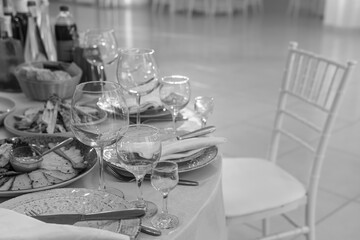 Table and chairs with wine glass, plates full serving. Napkins and cutlery. Low light. Selective focus. Ready to party, celebrate. Restaurant services, public catering enterprises. Black and white.