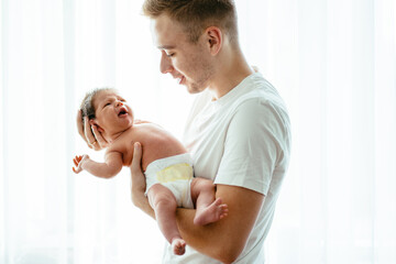 Parent love, tenderness concept. Portrait of father and son against light white background, caucasian white man holding his daughter on hands. Dad embracing his baby with love and care, smiling.