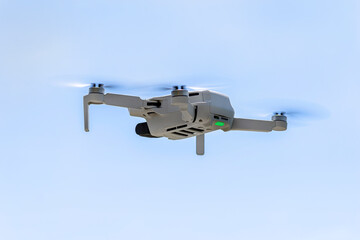 View of the hovering drone from rear against a blue sky background, the plastic propellers are on, visible green LED light.