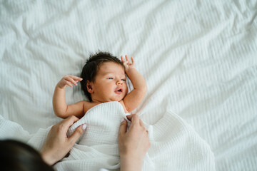 Newborn baby girl. Mothers hands calm down her mixed race newborn daughter on bed with white blanket. Family, love, calming, happy and new life concept.
