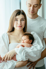 Vertically framed shot. Attractive woman and man holding a newborn. Mom, dad and baby. Portrait of smiling family with newborn on the hands. Happy family,parent love, tenderness concept.