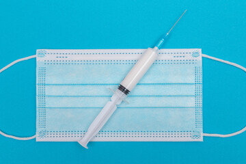 A Syringe and Face Mask on Blue Table - Top View. Syringe is Prepared for Vaccination or Injection. Medical Experiment. Blue Disposable Medical Mask. Virus protection - Flat Lay