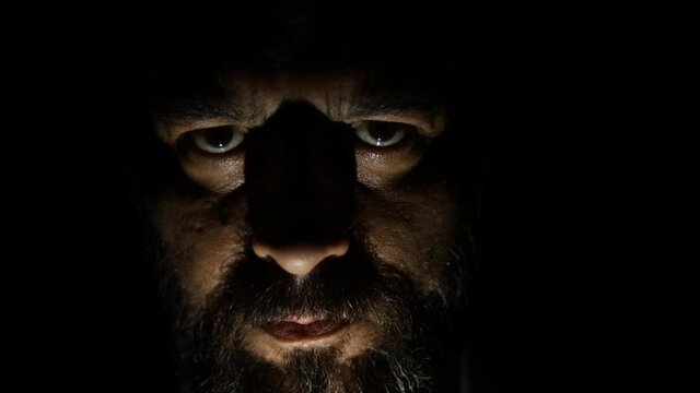 Bearded man in the dark looking at the camera. Low light in the dark.
