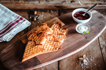 Deliciosos gofres en forma de corazón  con salsa de crema agria y mermelada de frambuesa presentado en bandeja de madera.