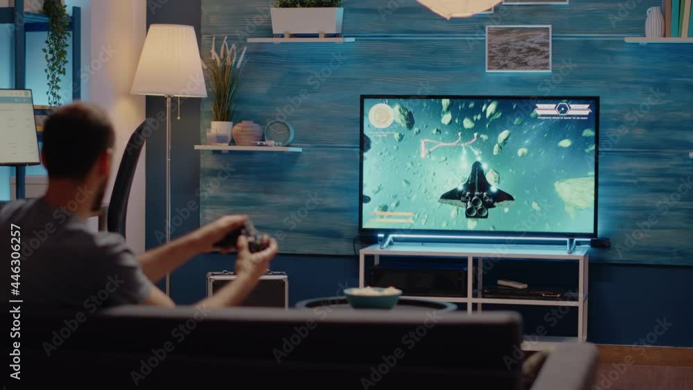 Poster caucasian man playing video games on tv console using joystick while sitting on couch in living room