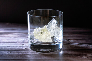 Empty whiskey glass with large chunks of ice is on a table with a black background.