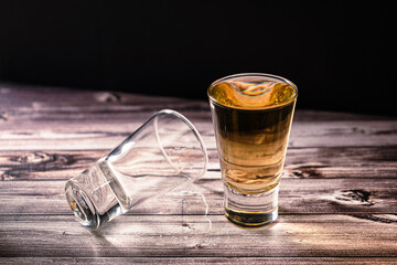 Horizontally oriented chopped view of a shot of whiskey or scotch or bourbon next to a second dropped shot.