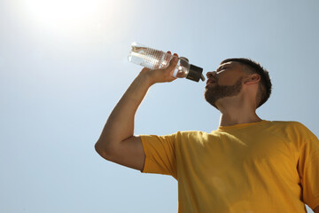 Man drinking water to prevent heat stroke outdoors, low angle view