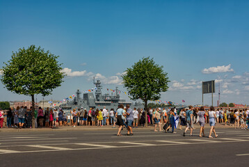 People walking along the embankment against the backdrop of the divorced Palace Bridge and warships. Rehearsal of the parade for the Day of the Russian Navy.