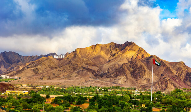 Hatta city welcoming sign written with large letters placed in Hajar mountains and UAE flag flying high in Hatta enclave of Dubai in the United Arab Emirates.