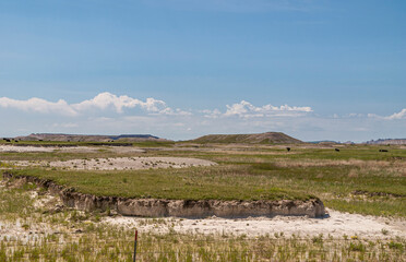 Badlands National Park, SD, USA - June 1, 2008: Green Prairie expanse with geologic deposits under...