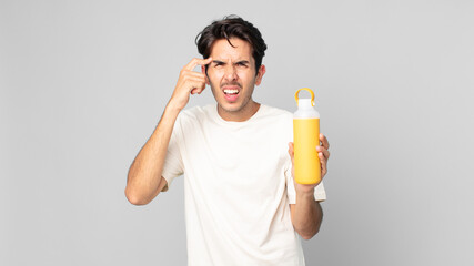young hispanic man feeling confused and puzzled, showing you are insane with a coffee thermos