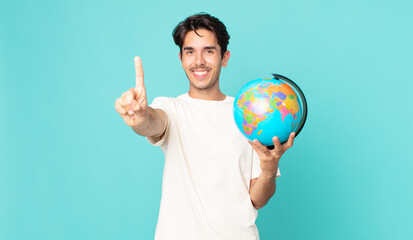 young hispanic man smiling and looking friendly, showing number one and holding a world globe map