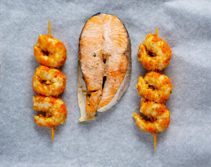 Food on baking paper. Food to be reheated in the oven. Salmon steak and shrimp skewers.