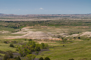 Fototapeta na wymiar Badlands National Park, SD, USA - June 1, 2008: Wide landscape of green prairie with white and beige geologic deposits cropping out under blue sky. Long ridge on horizon,