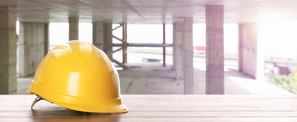 Hard hat on white wooden surface at construction site with unfinished building, banner design....