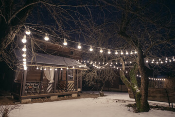 Wooden country house with a veranda on the plot in winter. Outside view. Lighting the site with a...