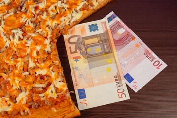 Pizza and money (euros) on a dark table.