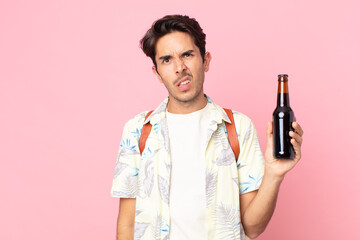 young hispanic man feeling puzzled and confused and holding a bottle of beer