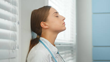 Attractive woman doctor breathes deeply leaning on wall