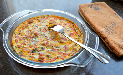 omelet with sausage and tomatoes in a glass dish, next to a kitchen towel