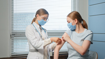 Blonde nurse in disposable facial mask and glasses injects young woman patient arm