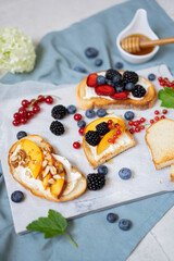 Toasted bread with cream cheese, honey, nuts, fruits and fresh berries. Summer tasty breakfast - dessert on white textured table. Selective focus with copy space.