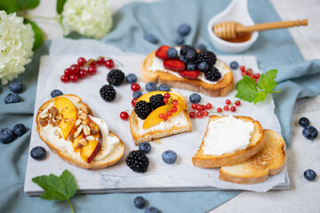 Toasted bread with cream cheese, honey, nuts, fruits and fresh berries. Summer tasty breakfast - dessert on white textured table. Selective focus with copy space.