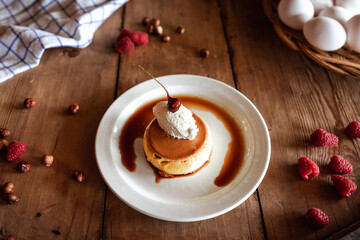 delicioso flan de huevo con nata y avellana caramelizada, sobre un plato blanco en una mesa de madera con avellanas y frambuesas.