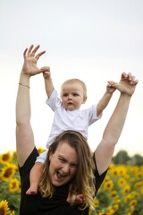 brunette woman young mom with cute baby blonde son on a field of sunflowers.