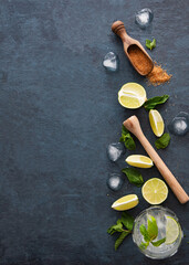 Concept flatlay with ingredients for mojito lemonade:  fresh lime slices, brown sugar, mint and ice on a dark blue  background. Top view and copy space