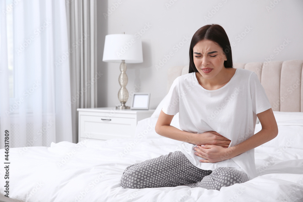 Poster Young woman suffering from stomach ache in bedroom