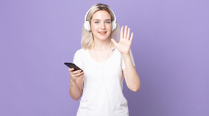 young pretty albino woman smiling and looking friendly, showing number five with headphones and...