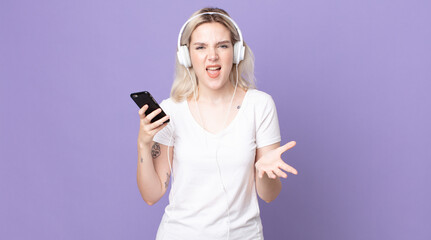 young pretty albino woman looking angry, annoyed and frustrated with headphones and smartphone