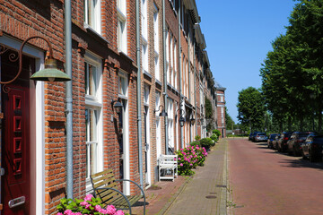 Fototapeta na wymiar Helmond, Netherlands - July 10. 2021: View on street with red asphalt and typical dutch old houses in summer with blue sky