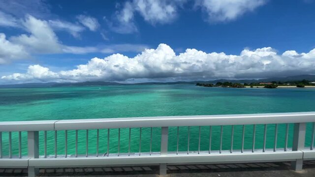 OKINAWA, JAPAN - JUNE 2021 : Driving at Kouri Island bridge. Wide camera point of view (POV), seaside road driving shot. Blue sunny summer sky.