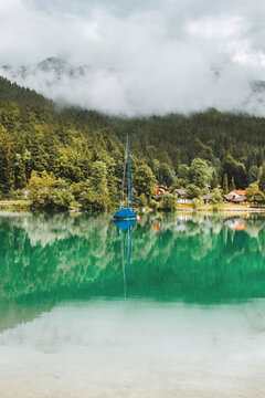 Morning on the lake in Bavarian Alps. Sail boat. Clouds in mountains, Germany. Beautiful landscape with reflection in calm water. Outdoor relaxing photo.