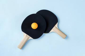 Two black ping pong paddles and one yellow ball