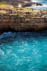 Fototapeta na wymiar People stand close to a cliffside in Polignano a Mare in the Puglia region of Italy.