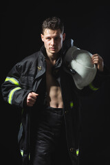 Fototapeta na wymiar Portrait of a young man in fire equipment on a black studio background. Fireman in a dark uniform.
