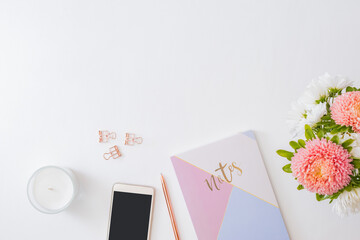Flat lay home office desktop with smartphone, flowers in a vase, office supplies on a light background