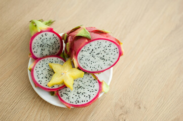 Slices of dragon fruit or pitaya with white pulp and black seeds on white plate with one slice of...