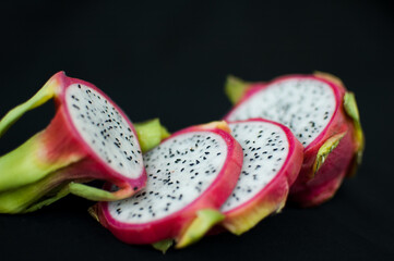 Slices of dragon fruit or pitaya with pink skin and white pulp with seeds on black background....