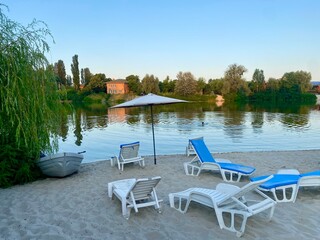 view of the river bank with empty sun beds and a boat