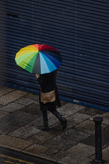 Woman walking with rainbow umbrella on street in city