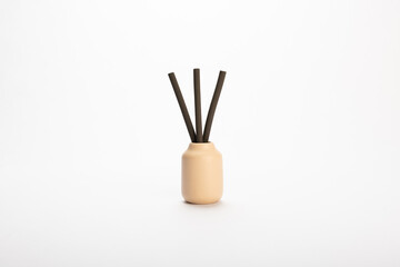 a cream colored ceramicdiffuser jar with brown scented reeds on white background