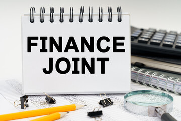 On the table is a magnifying glass, pencils, diaries and a notebook with the inscription - FINANCE JOINT